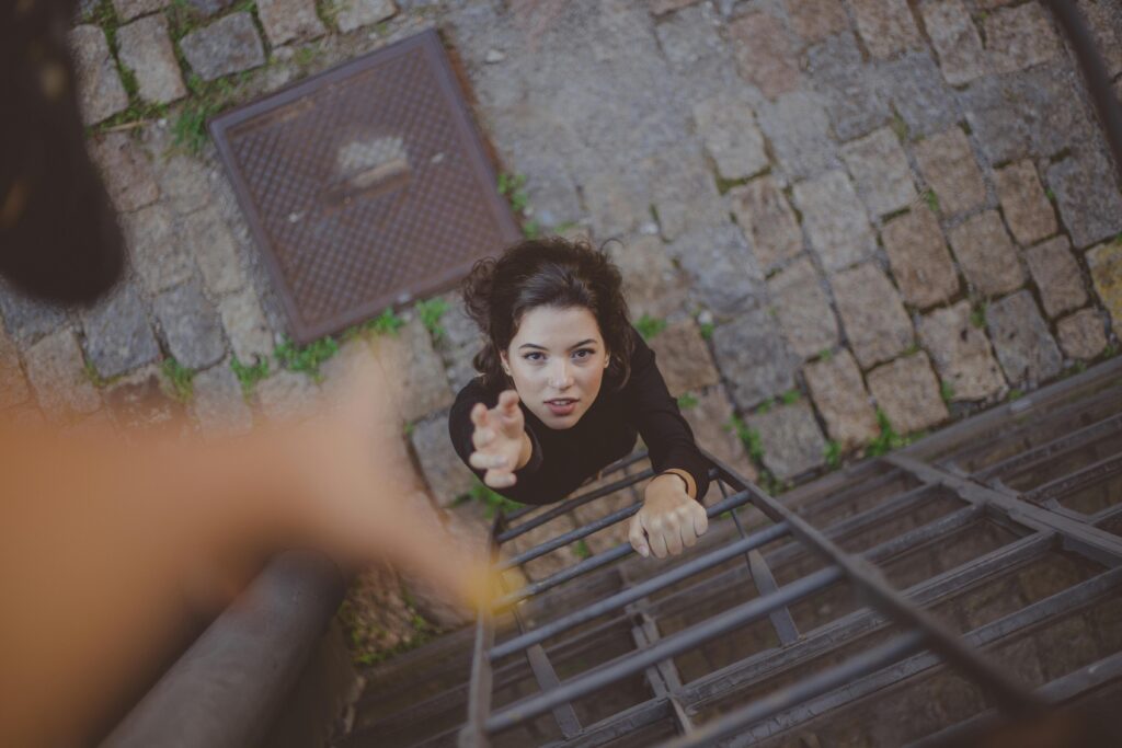 Woman climbs iron ladder outdoors, reaching for help with determination.